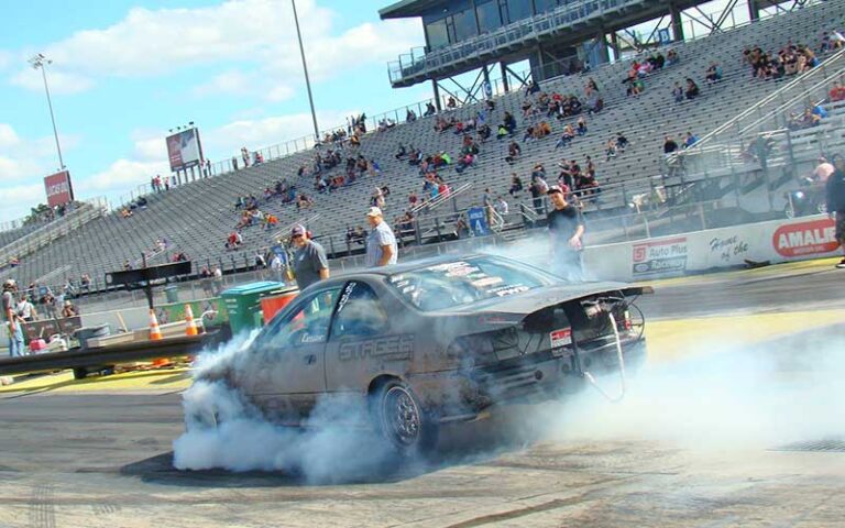 dragster car spinning tires with smoke and spectator stands at gainesville raceway