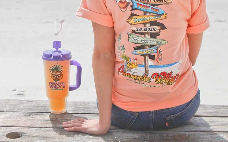 lady wearing merch shirt on beach with drink at pineapple willys panama city beach