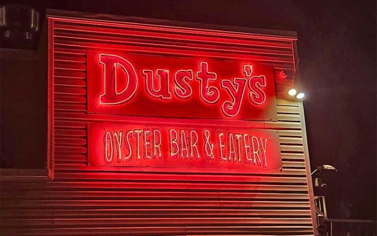 red neon sign on exterior at night at dustys oyster bar panama city beach