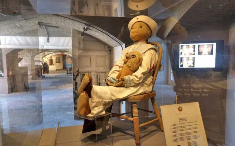 antique doll seated on chair inside glass case exhibit at fort east martello museum key west