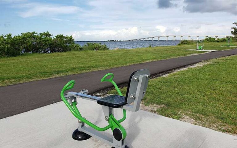 exercise machines along paved trail with bridge and bay view at sand point park titusville