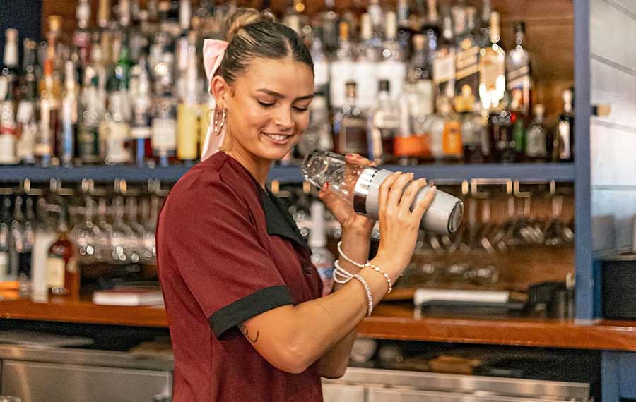 female bartender shaking cocktail behind bar with bottles on shelf in background at capt andersons panama city beach