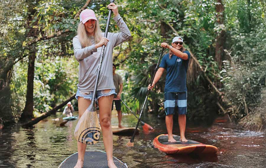 man and woman stand up paddleboarding along shady overgrown waterway at three brothers adventure tours daytona beach