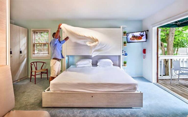 man making king bed in guestroom with balcony at nyah key west