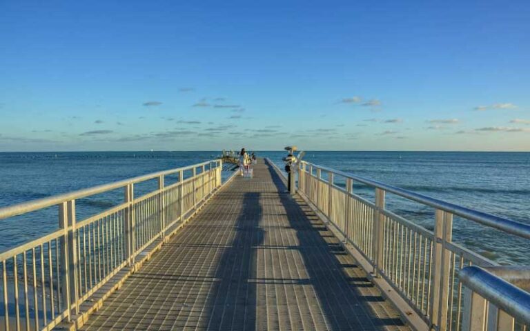 metal pier extending into ocean with people walking and clear sky at clarence s higgs memorial beach key west