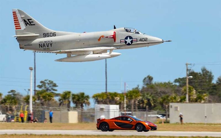 military plane flying over red sports car at valiant air command warbird museum space coast