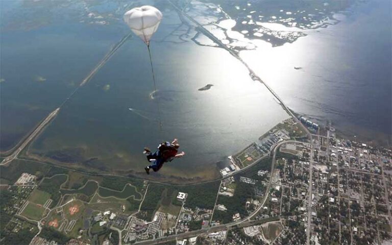 skydivers opening chute over aerial of coastline at skydiving space center titusville