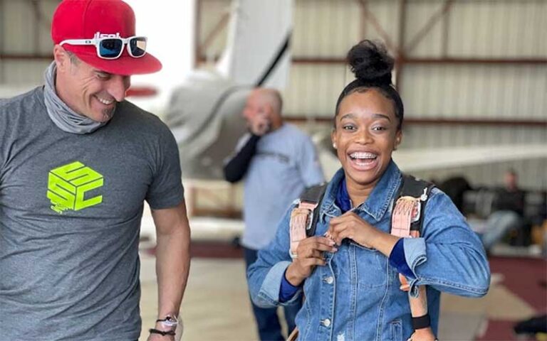 smiling girl putting on harness with instructor in hangar at skydiving space center titusville